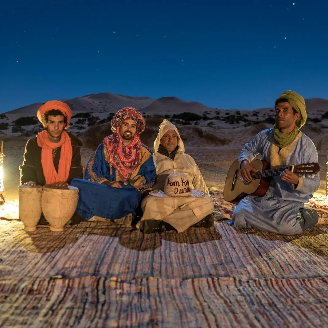Espacio representativo del hotel: Varias personas están sentadas sobre alfombras al aire libre mientras una toca la guitarra.