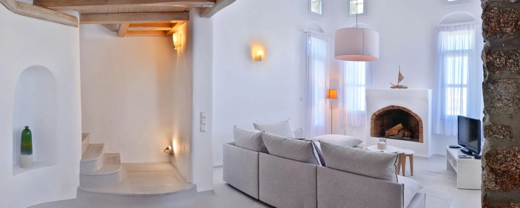 A bright living room with seating, tall windows, and a fireplace.