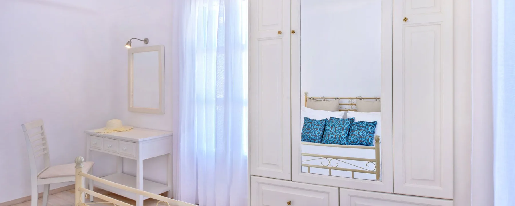 A bright bedroom with a bed and a small dressing table beside a window.