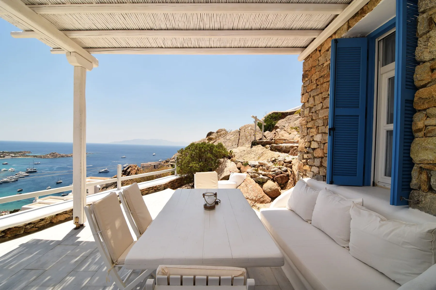 A shaded seaside terrace with outdoor seating and a view of the water.