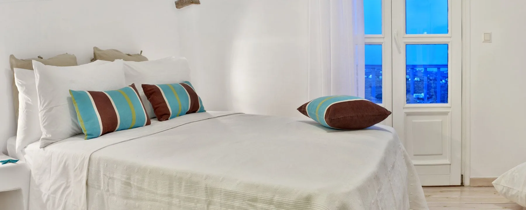 A bedroom with a bed dressed in white linens and colorful accent pillows.