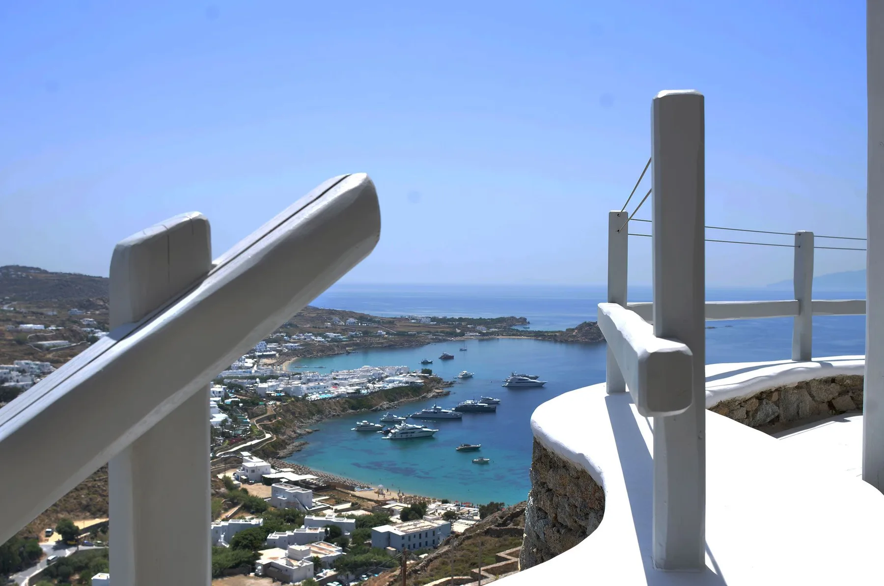 A coastal overlook shows a harbor and boats beyond a white railing.