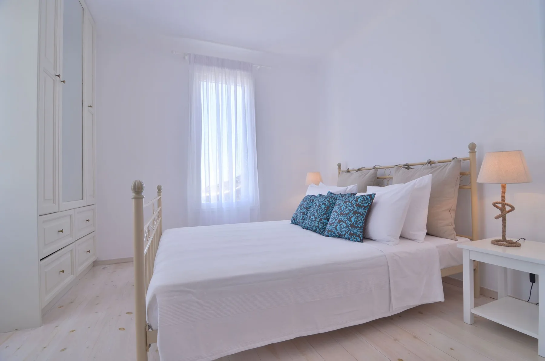 A bright bedroom with a neatly made bed and a curtained window.