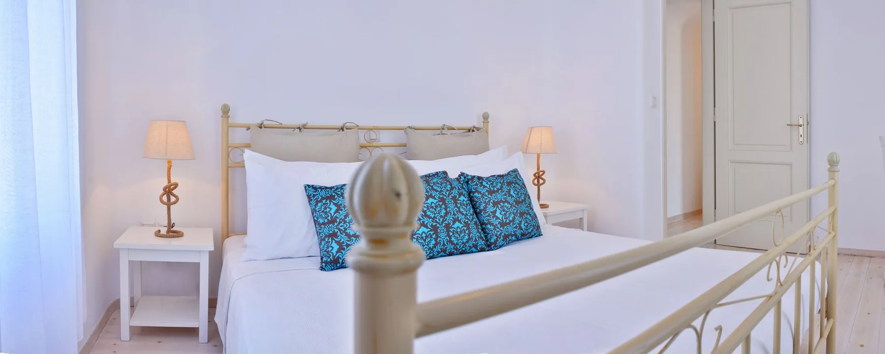A bright bedroom with a bed dressed in white linens and patterned blue cushions.