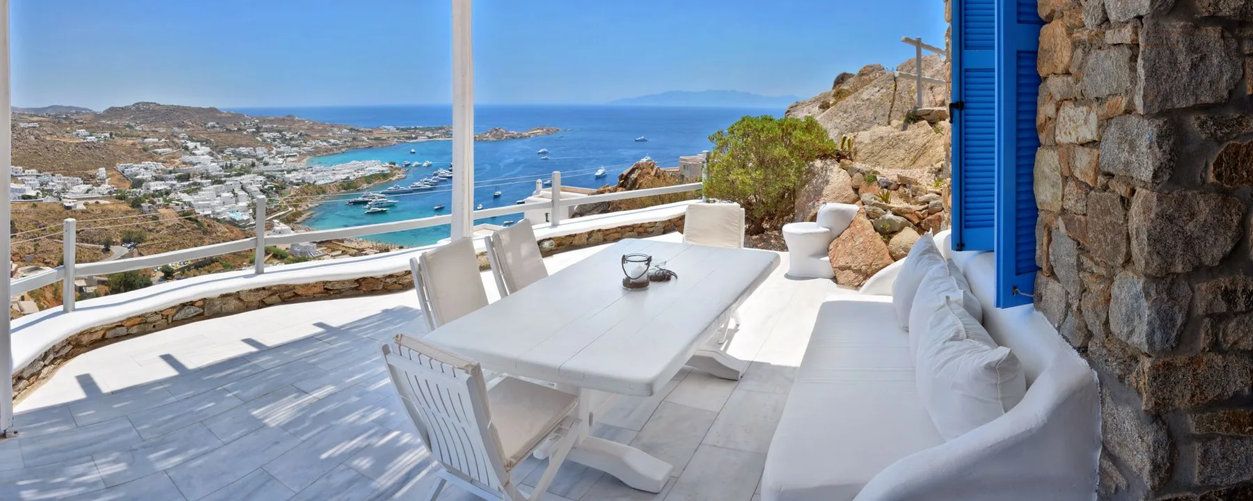 A seaside terrace with white outdoor seating and a table overlooking the coast.