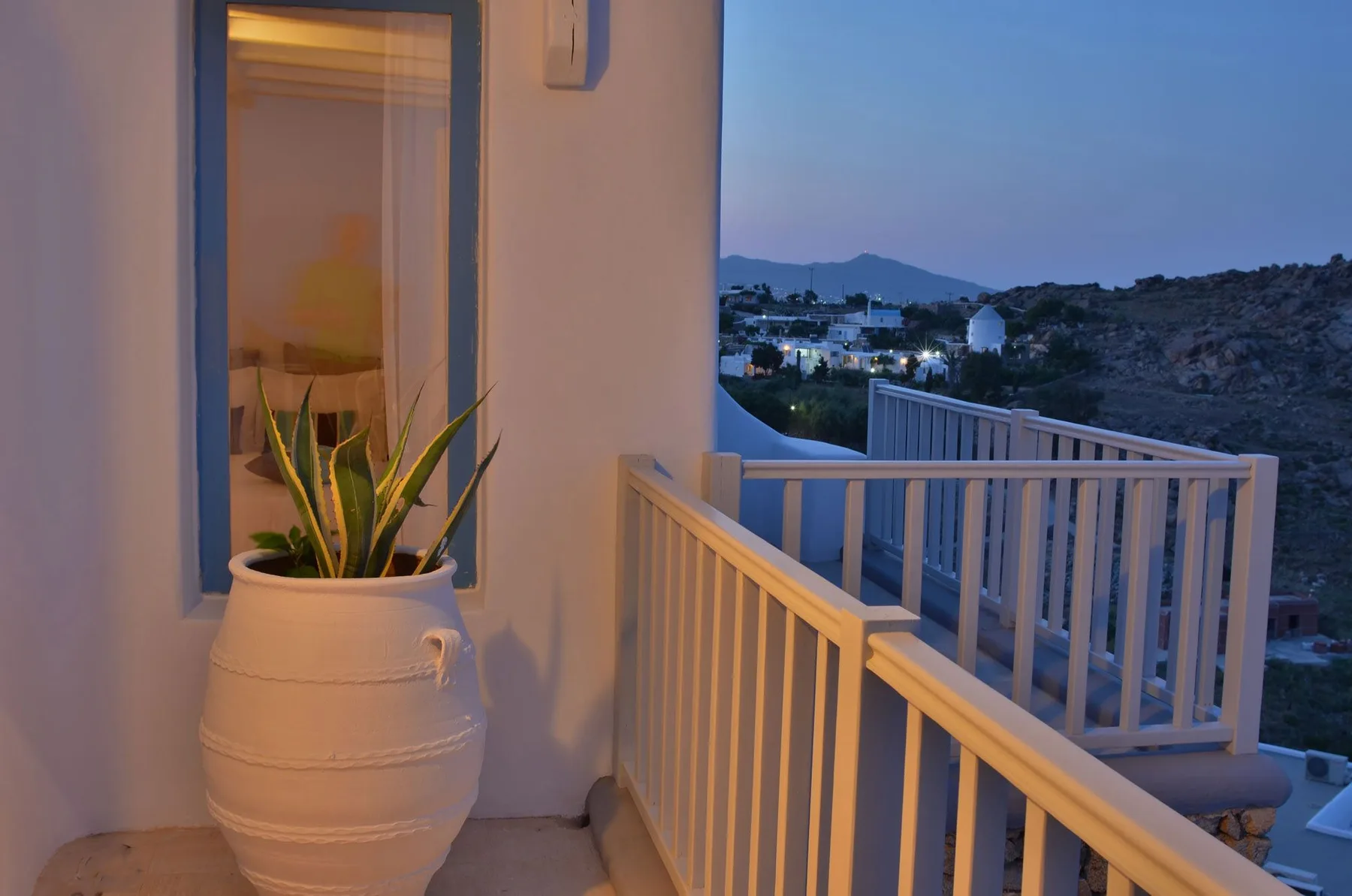 A balcony with white railings overlooks hillside homes at dusk.