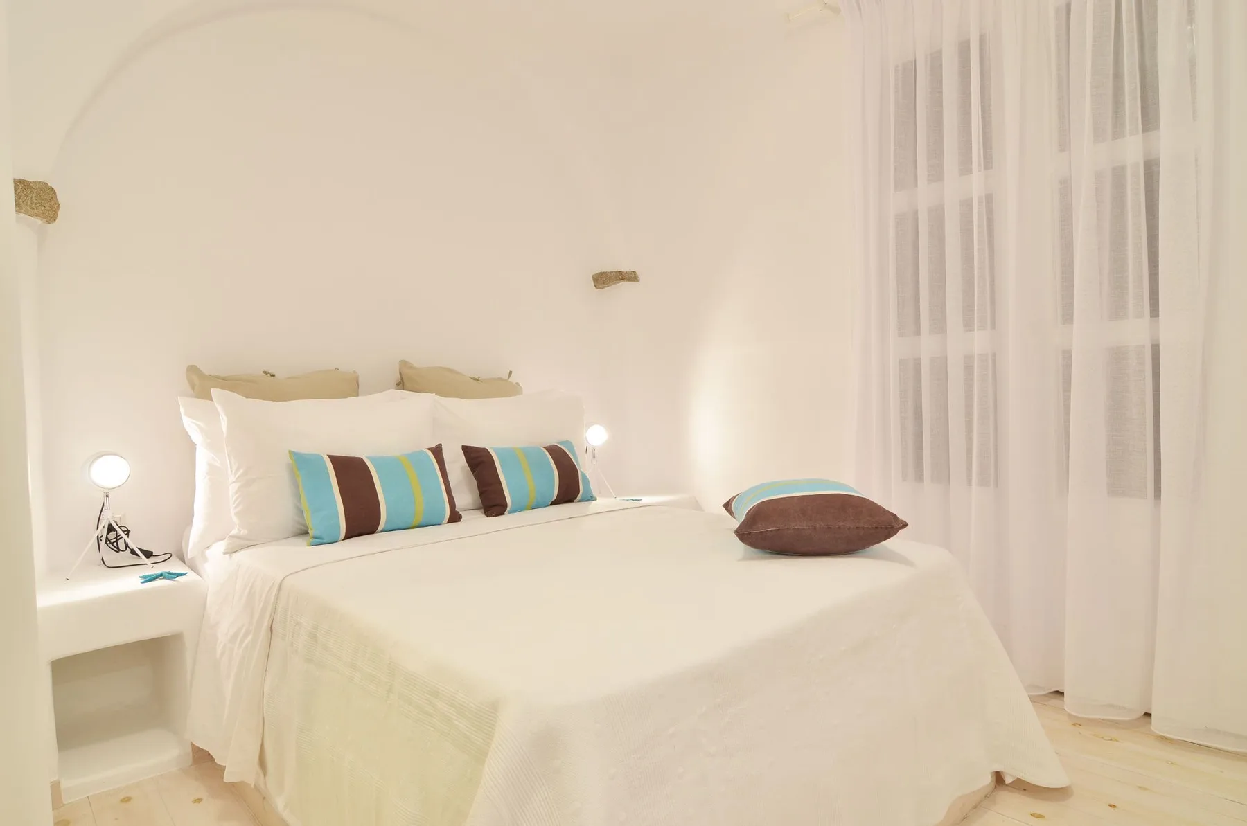 A bright bedroom with a neatly made bed and sheer curtains.