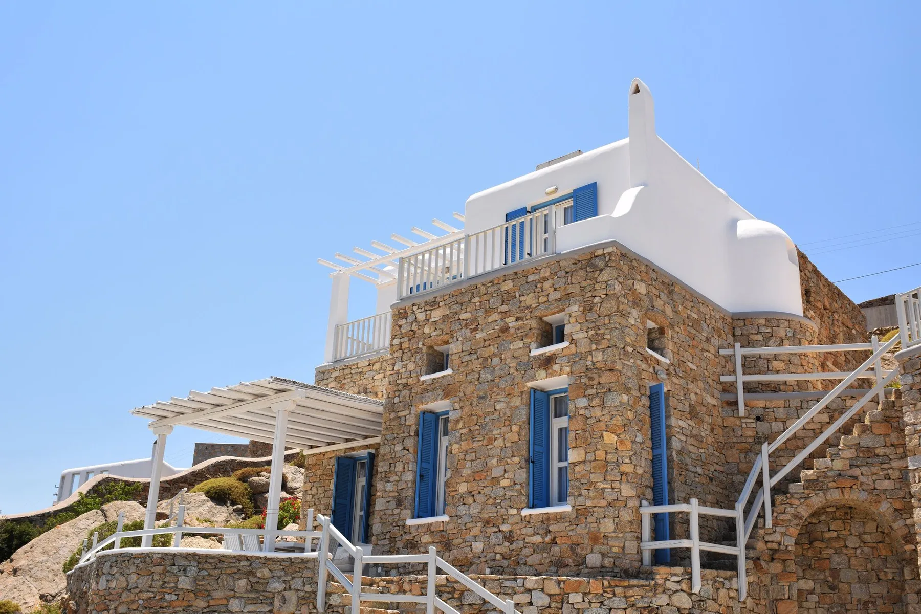 A stone building with white railings and a small upper terrace under a clear sky.