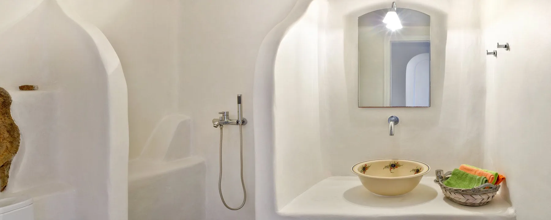 A white bathroom vanity with a vessel sink, mirror, and wall-mounted shower.