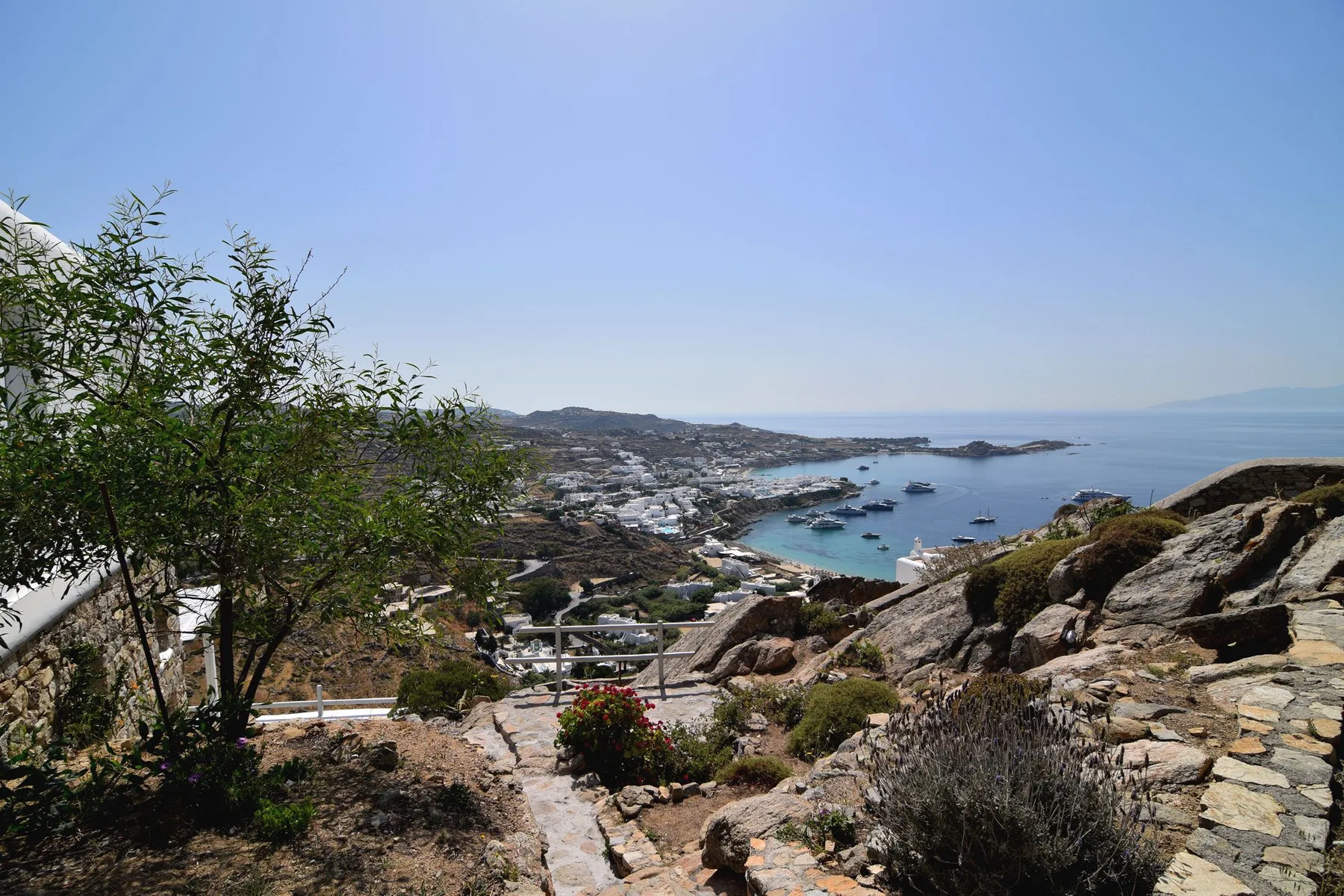 A coastal hillside overlooks a bay with boats and buildings along the shore.