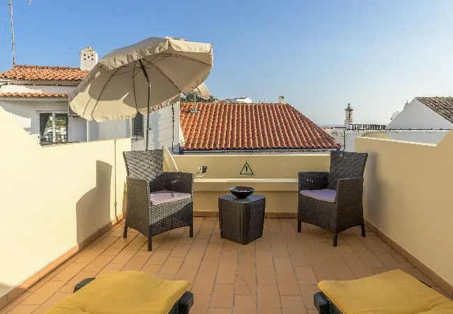 A sunny rooftop terrace has seating beneath a large umbrella.
