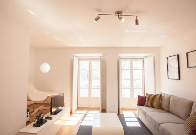 Una sala de estar luminosa con asientos junto a dos ventanas altas.