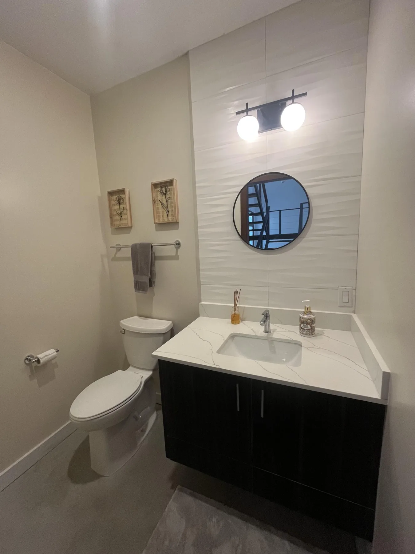 A bathroom with a vanity, round mirror, and toilet.