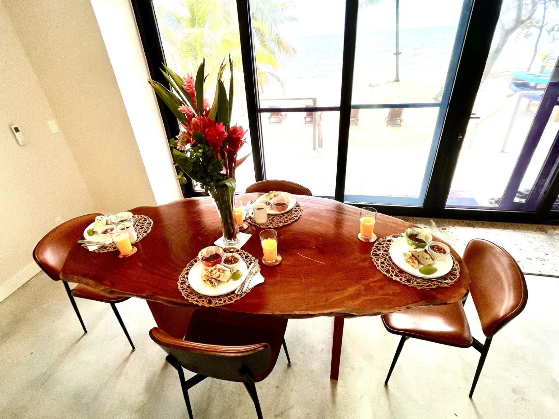 A dining table is set with plates and flowers beside large windows.