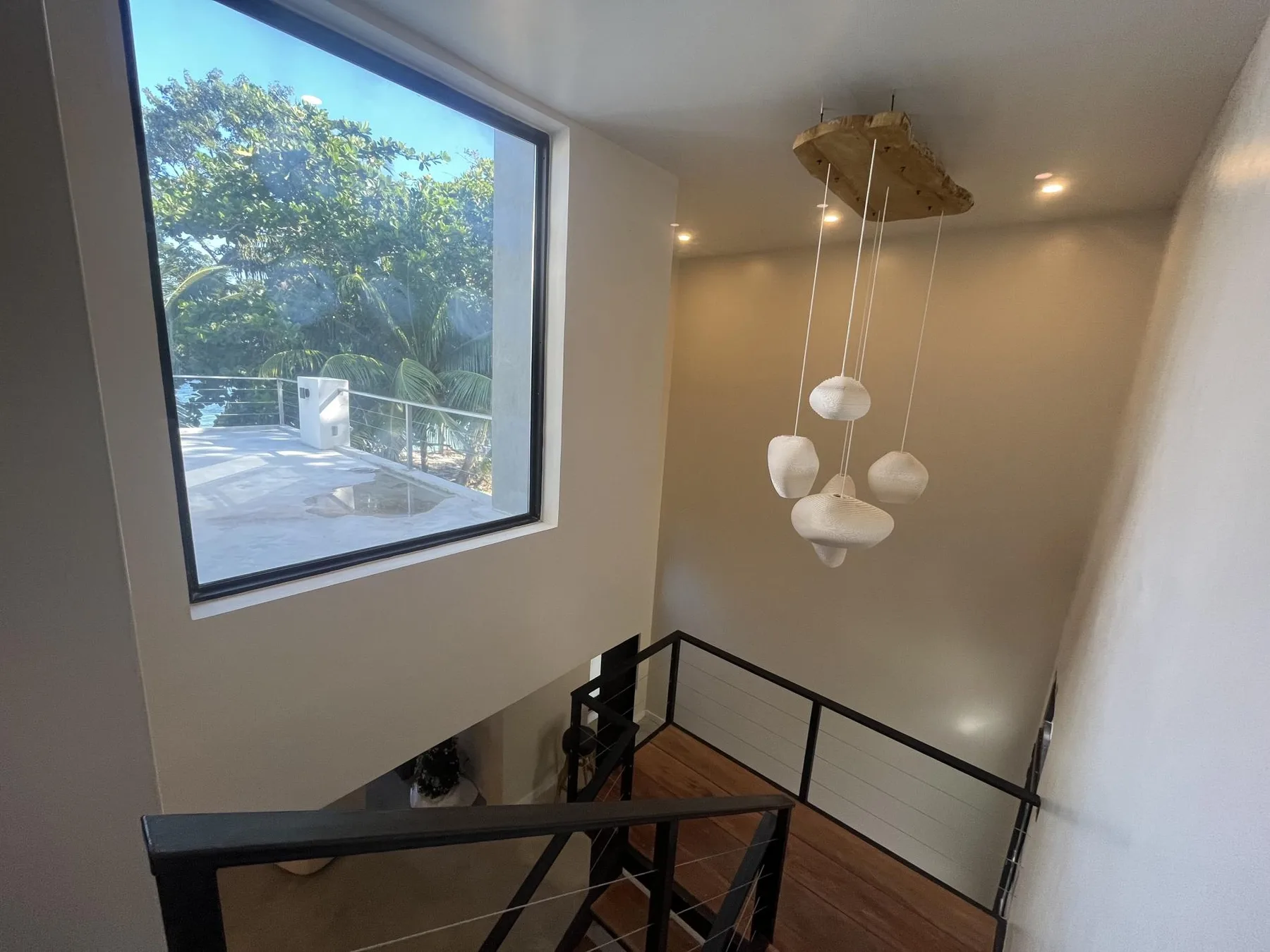 A stair landing with black railings and a large window overlooking greenery.