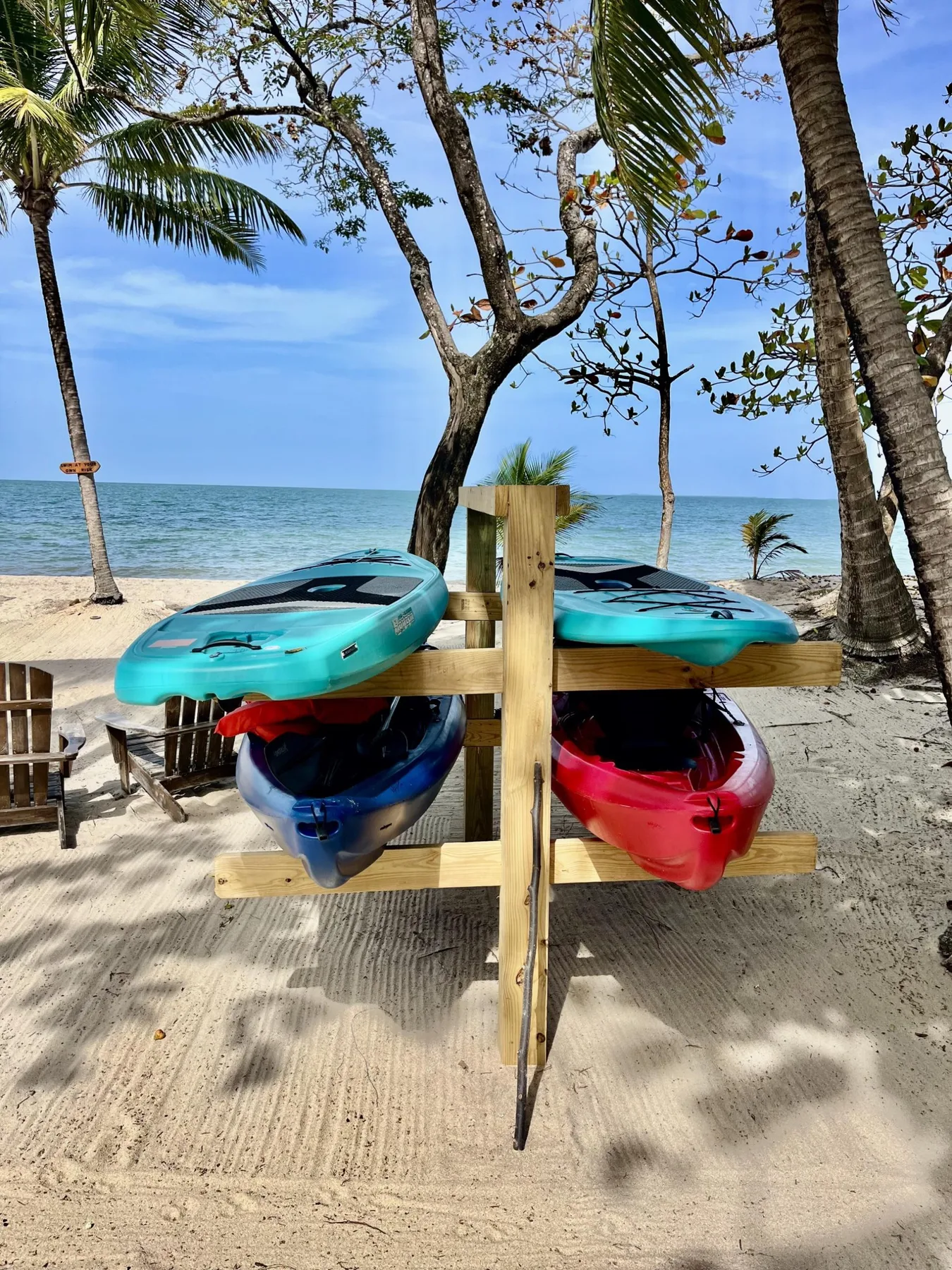 Kayaks are displayed on a wooden rack beside a sandy beach and the sea.