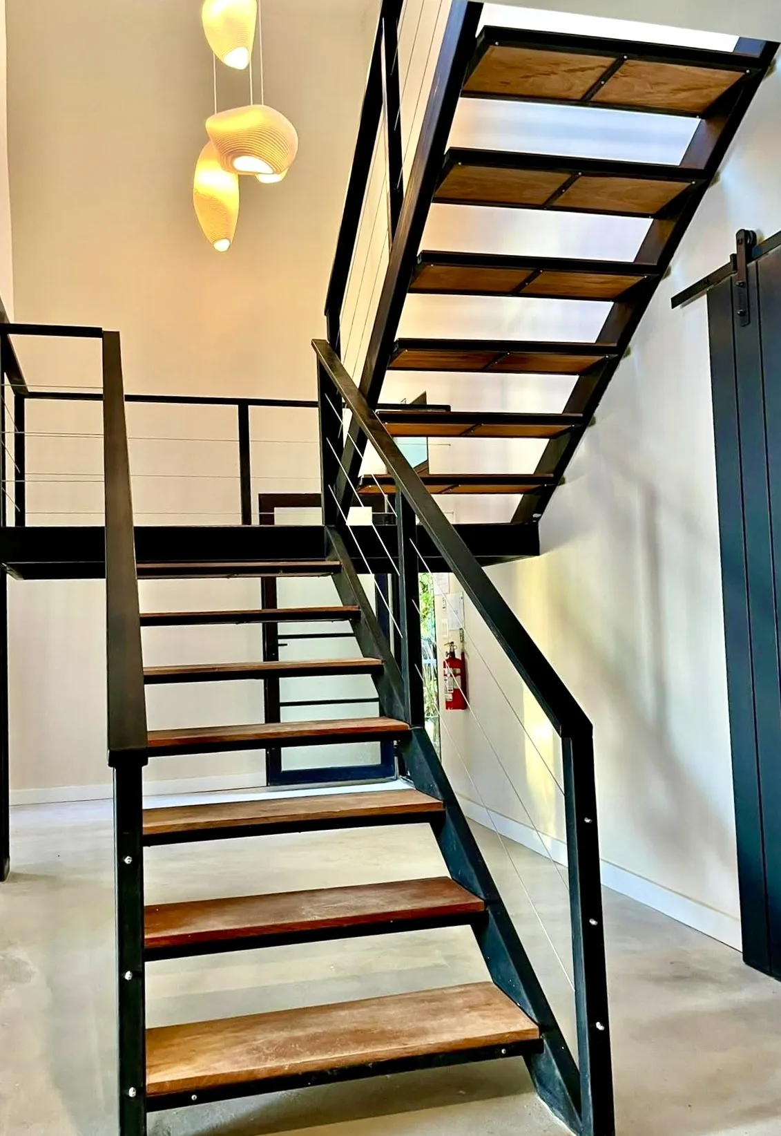 A modern interior staircase with wooden treads and dark metal railings.