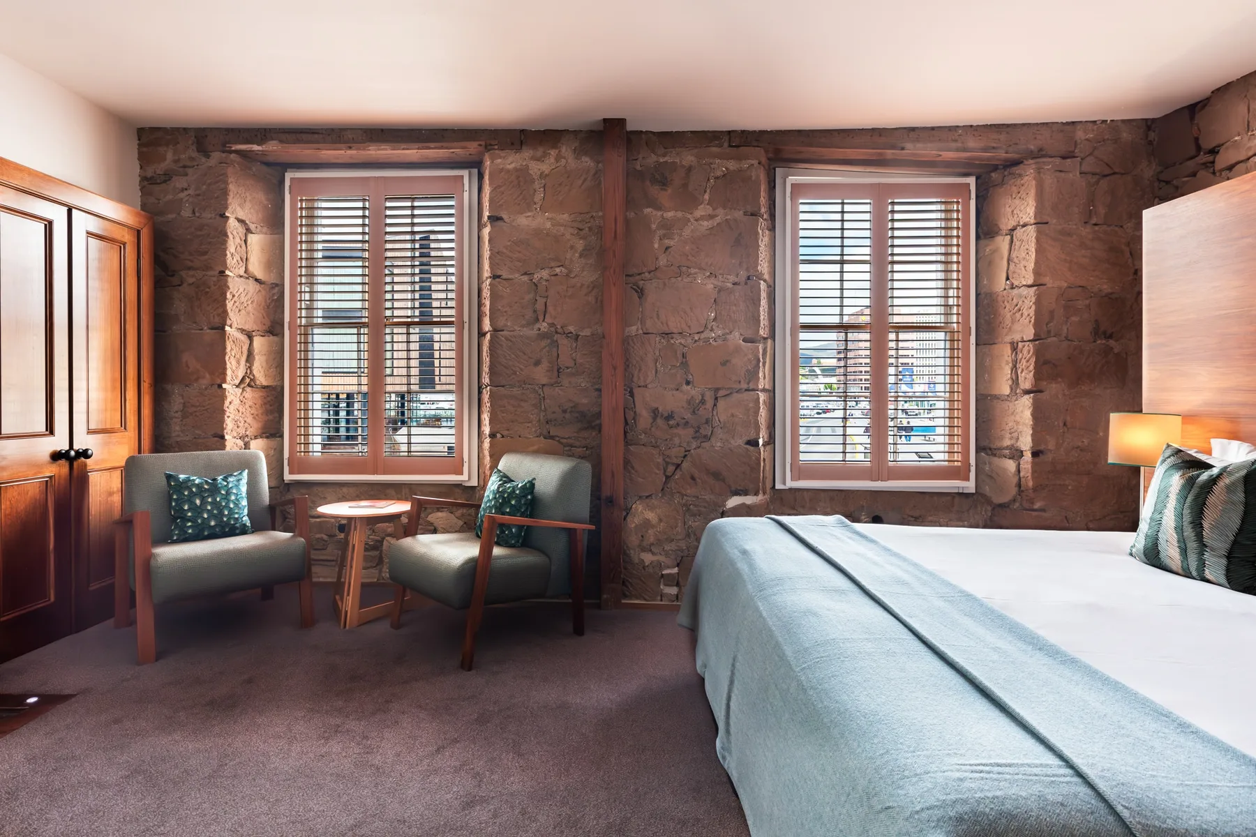 Representative hotel space: A bedroom with a bed, two armchairs, and windows set in a stone wall.