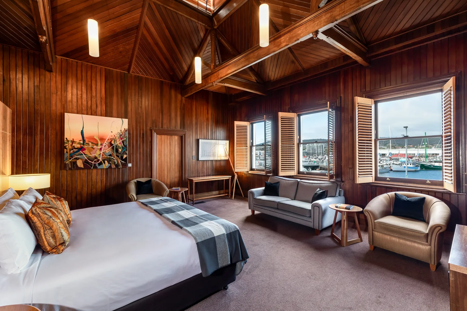Representative hotel space: A wood-paneled bedroom has a bed and seating beside windows overlooking a harbor.