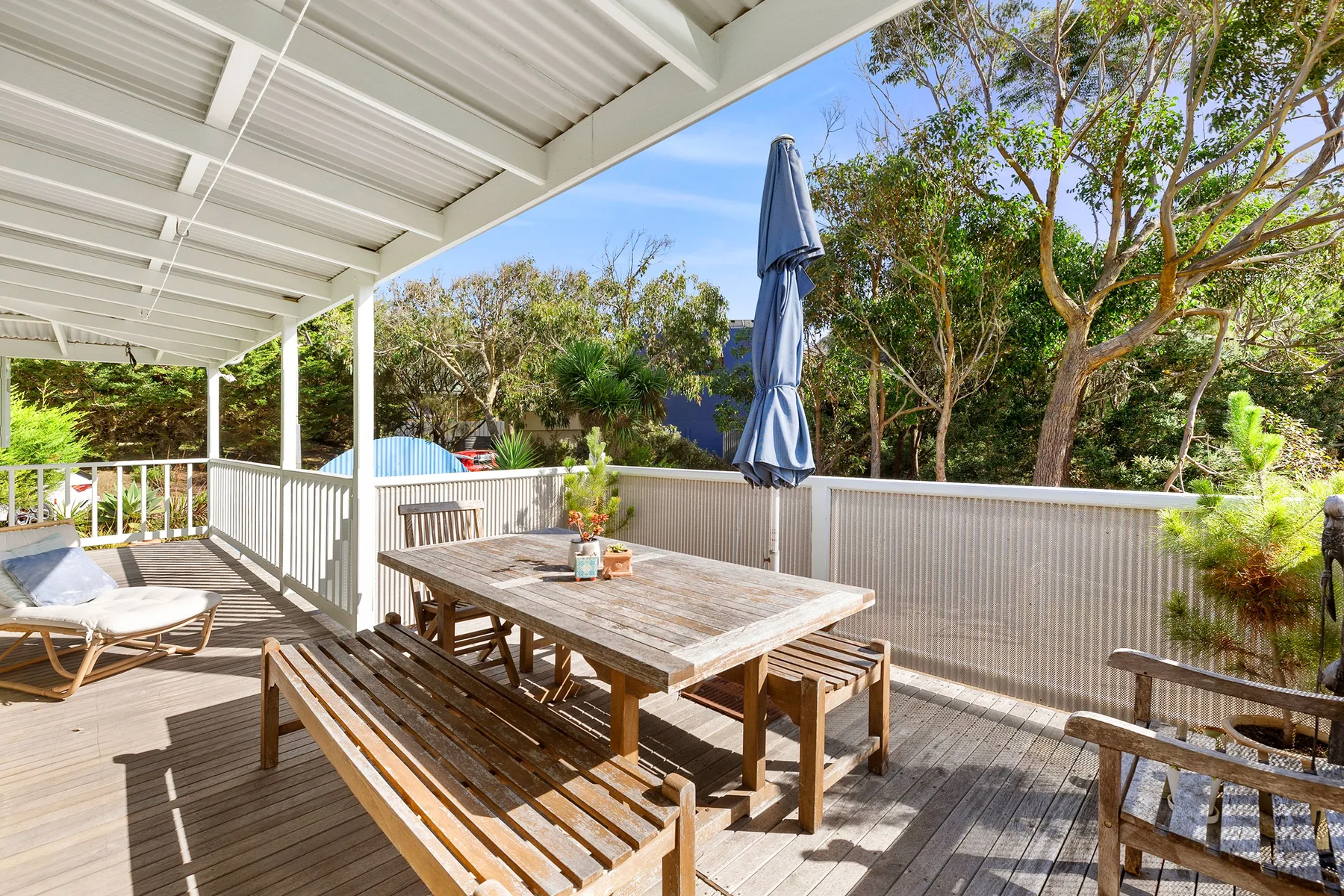 A covered wooden deck with a dining table and seating overlooks trees.