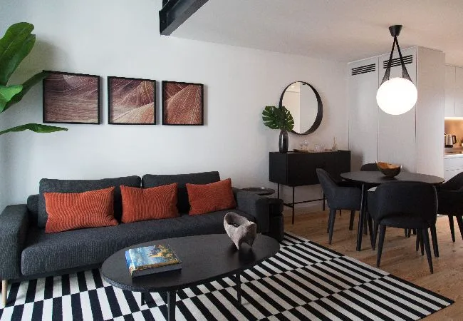 Una sala de estar y comedor con sofá oscuro, mesa y alfombra a rayas.