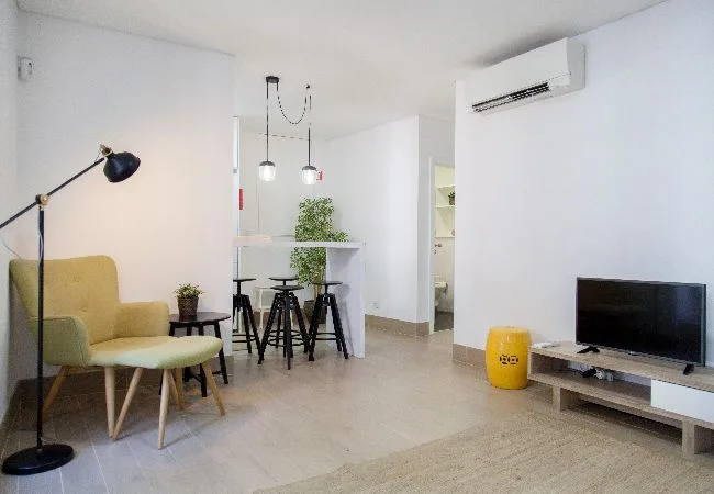 A bright living area with seating, a dining counter, and a television.