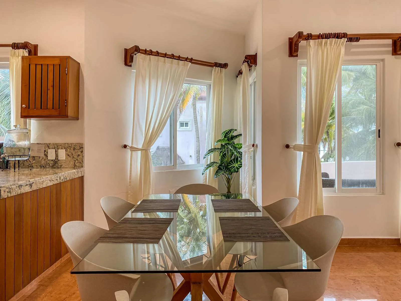 Un comedor con una mesa de vidrio y sillas junto a ventanas con cortinas.