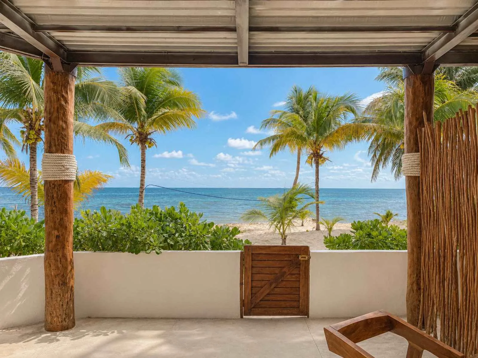 Un patio sombreado da a una playa con palmeras y el océano.