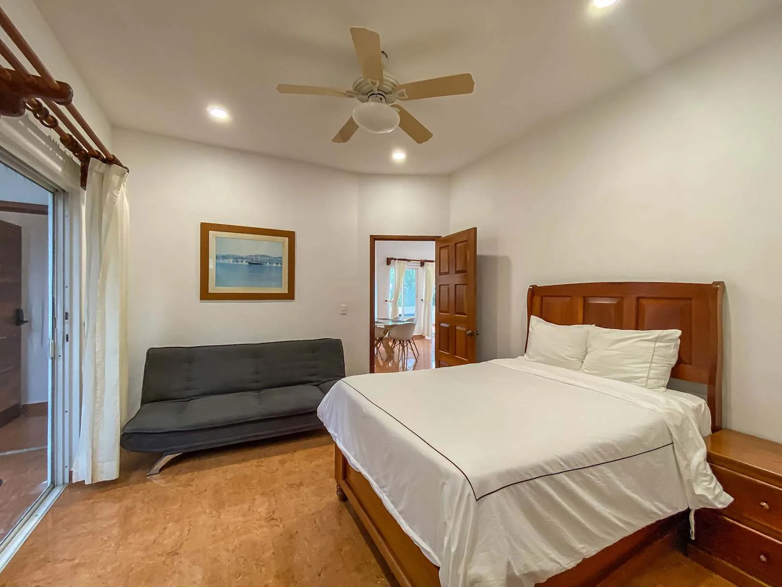 Un dormitorio con una cama bien hecha, un sofá gris y una puerta abierta.