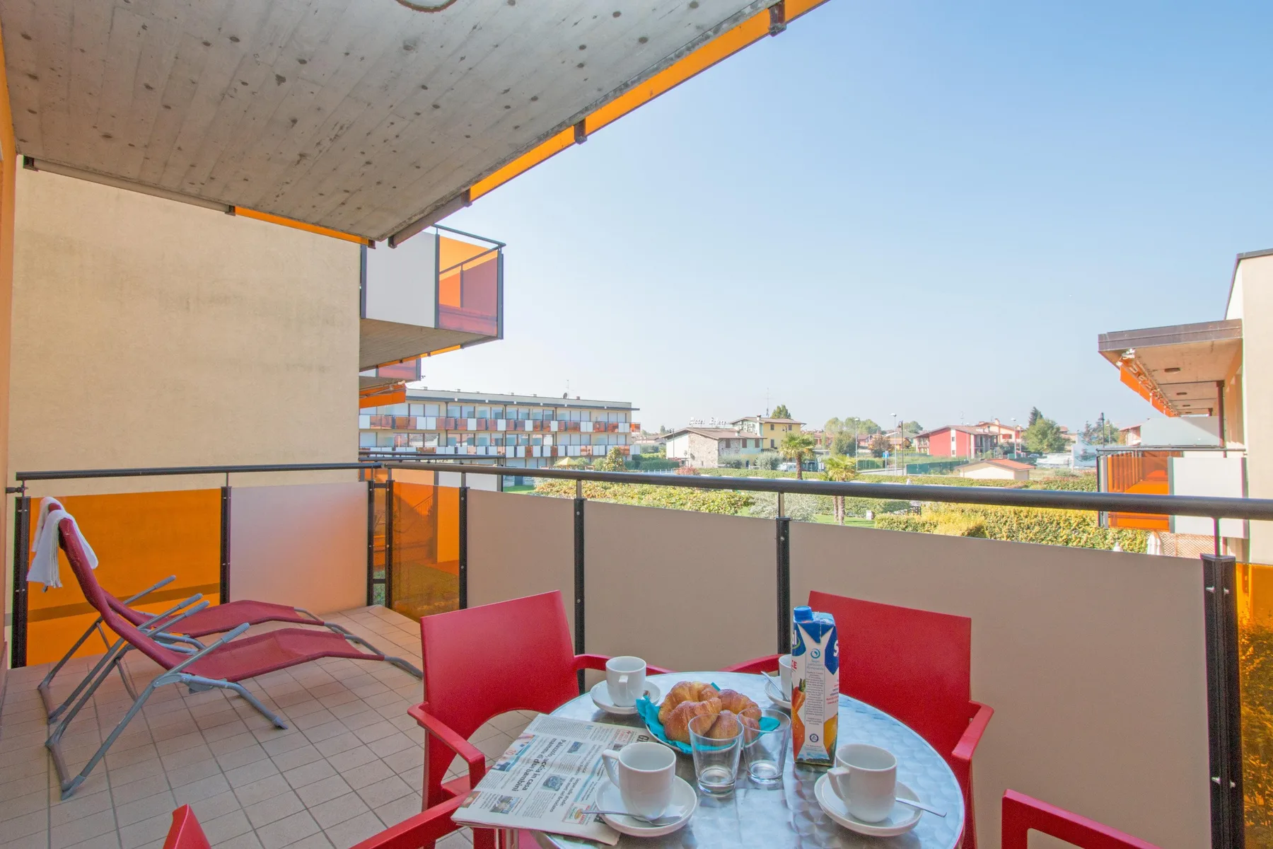 A covered balcony with red seating and a small table overlooks nearby buildings.