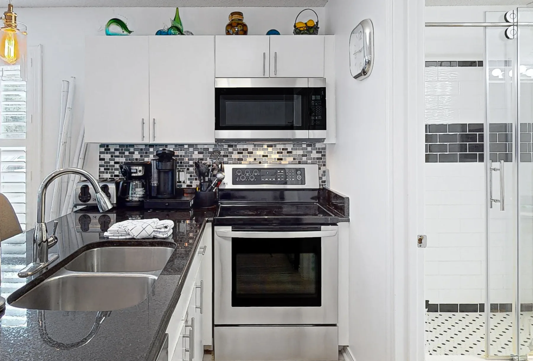 Una cocina luminosa con gabinetes blancos, encimeras oscuras y electrodomésticos de acero inoxidable.