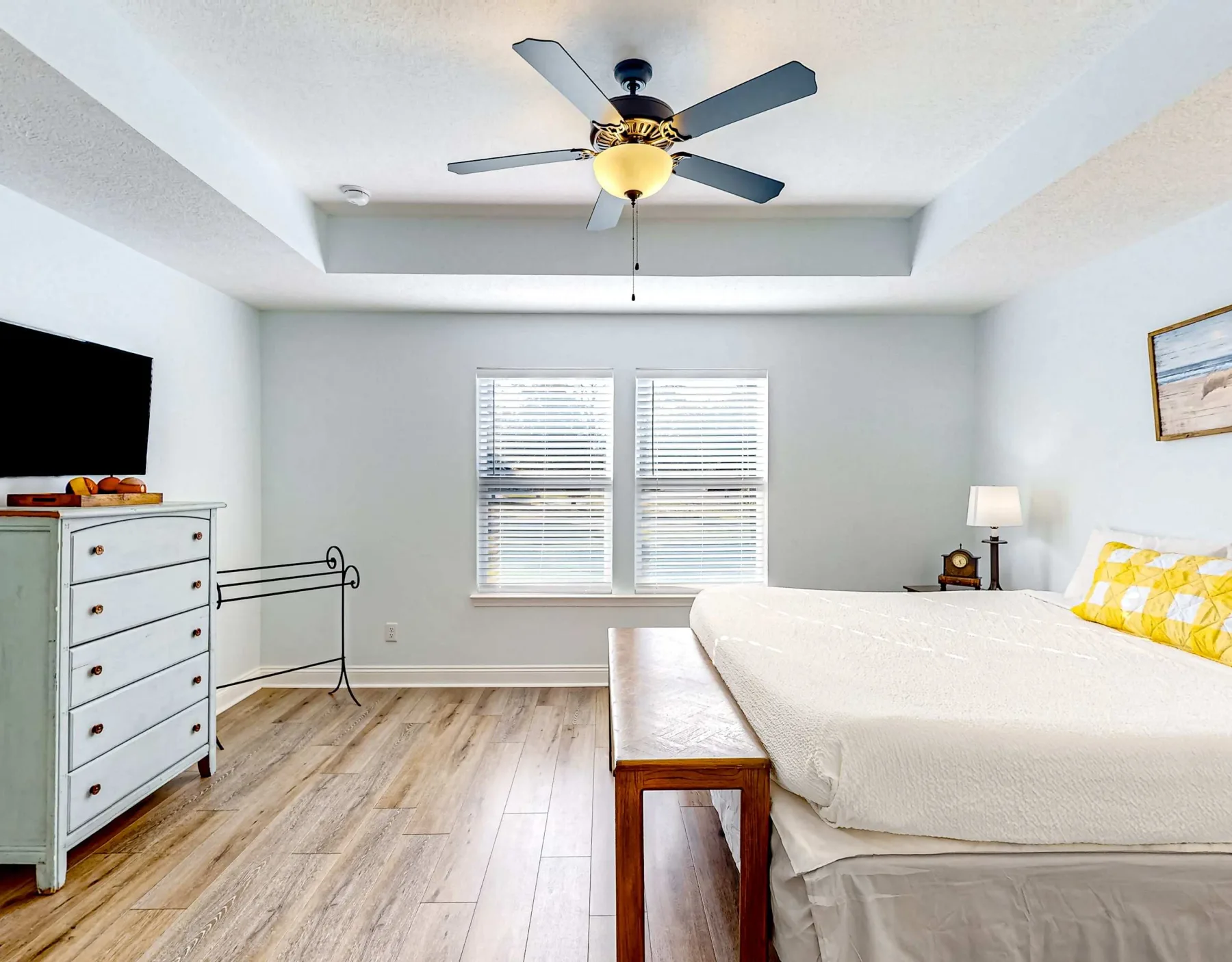 Un dormitorio luminoso con una cama, dos ventanas y un ventilador de techo.