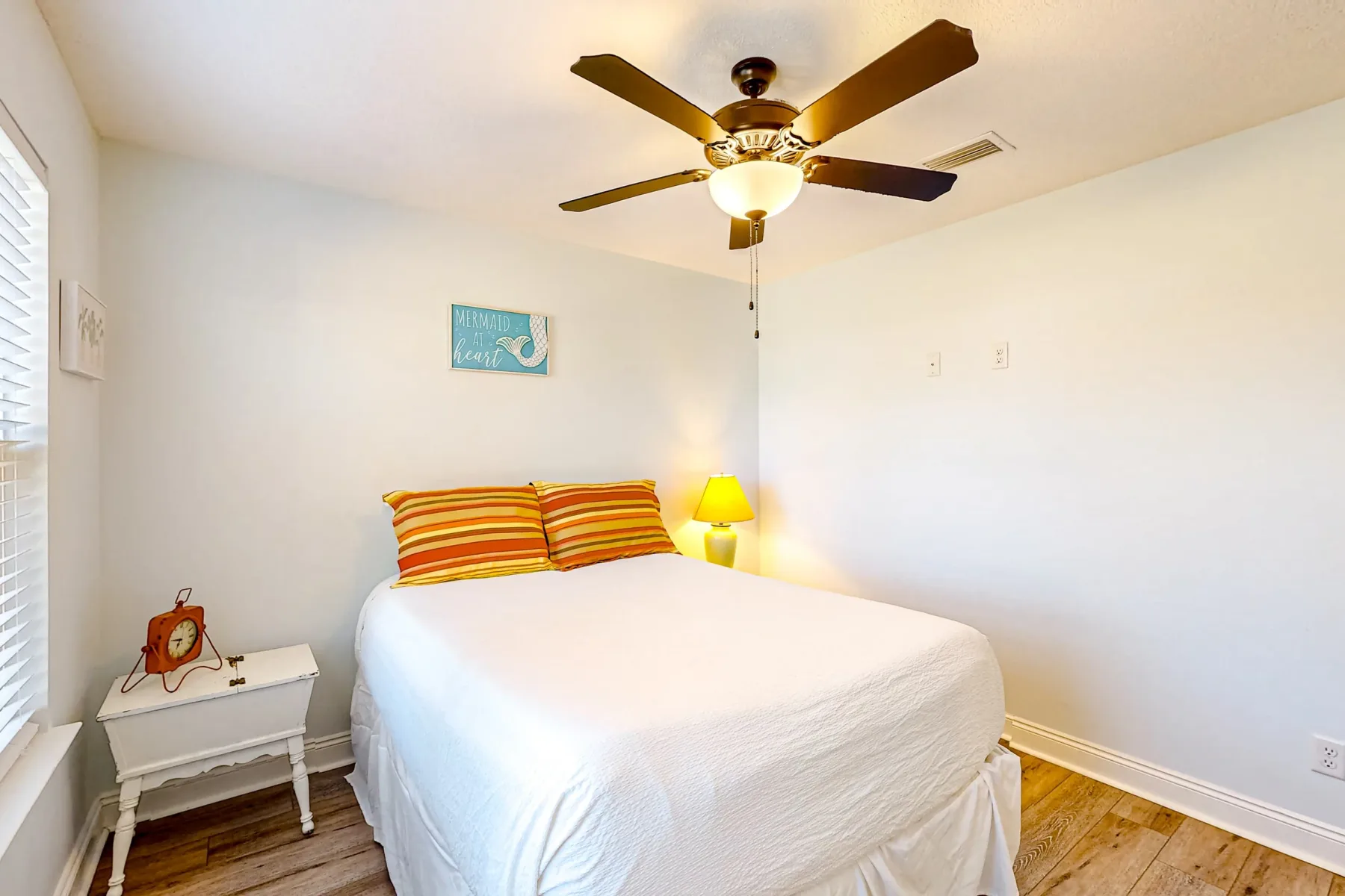 Un dormitorio con una cama blanca, almohadas a rayas y un ventilador de techo.