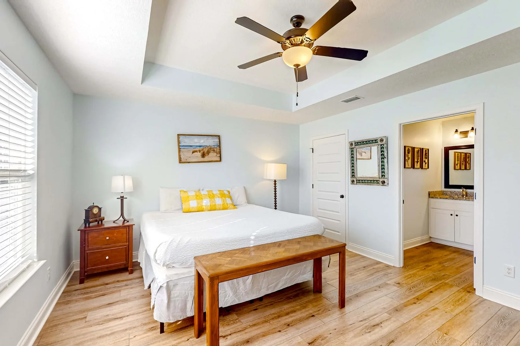 Un dormitorio luminoso con una cama bien tendida y una mesa de madera a sus pies.