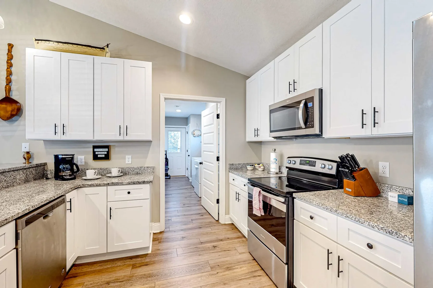 Una cocina luminosa con gabinetes blancos, encimeras de piedra y electrodomésticos de acero inoxidable.