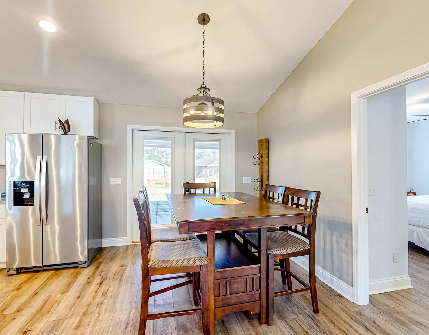 Comedor con una mesa de madera y sillas junto a un refrigerador de acero inoxidable.