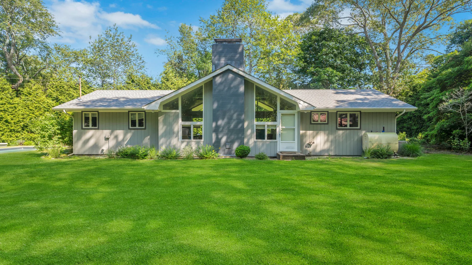 A single-story house with a central chimney stands behind a broad green lawn.