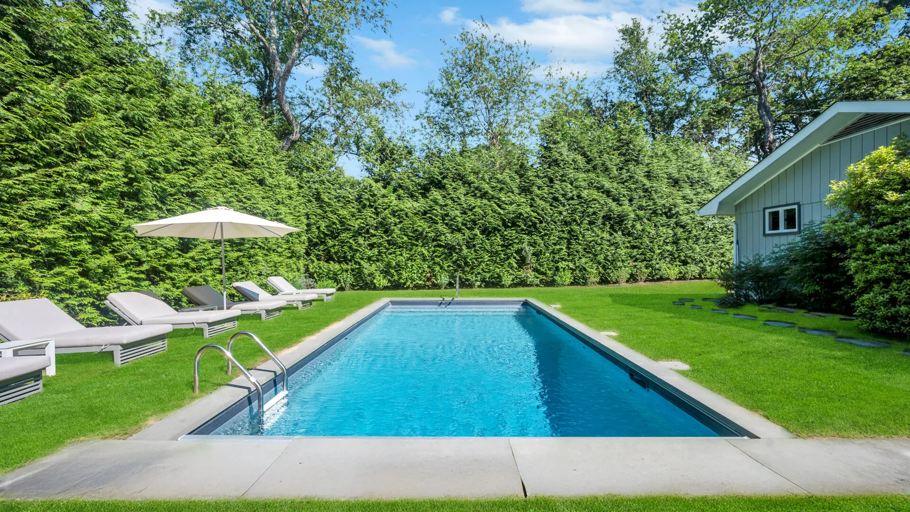 An outdoor swimming pool sits in a green lawn, with lounge chairs nearby.
