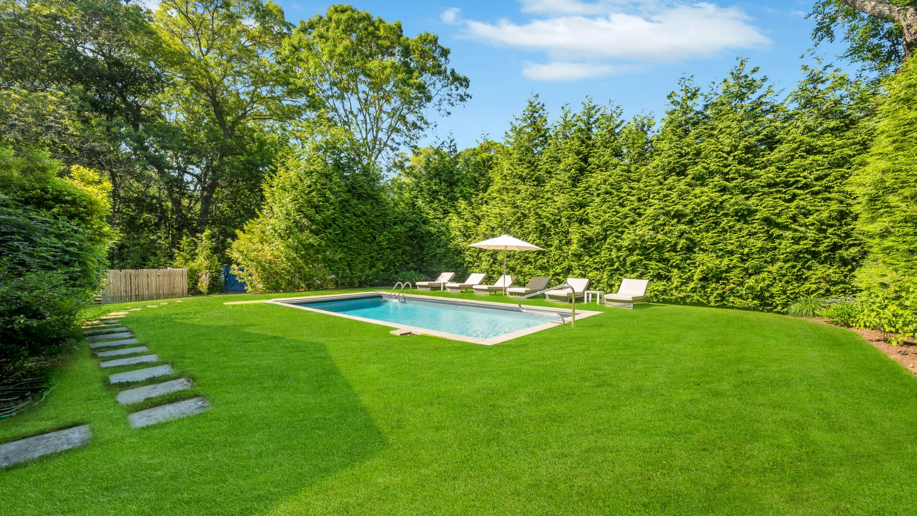 A swimming pool sits beside a broad lawn, with lounge chairs and trees nearby.