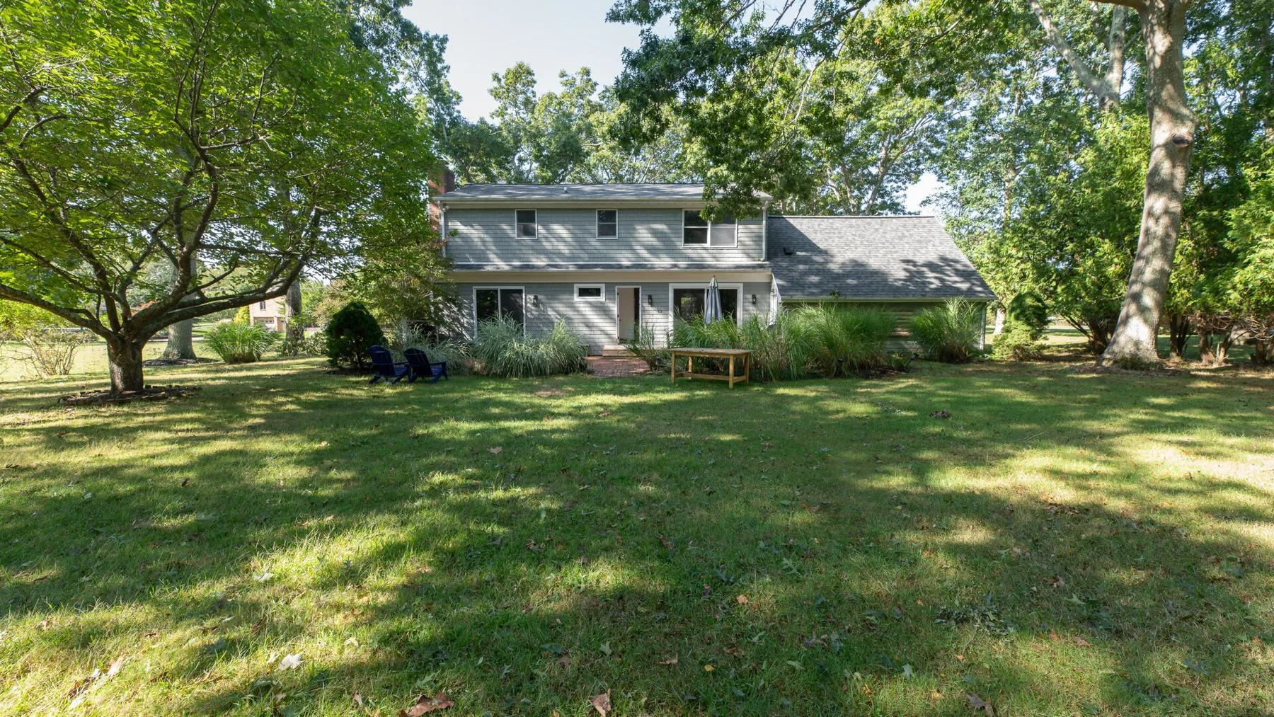 A two-story house stands behind a broad grassy yard and mature trees.