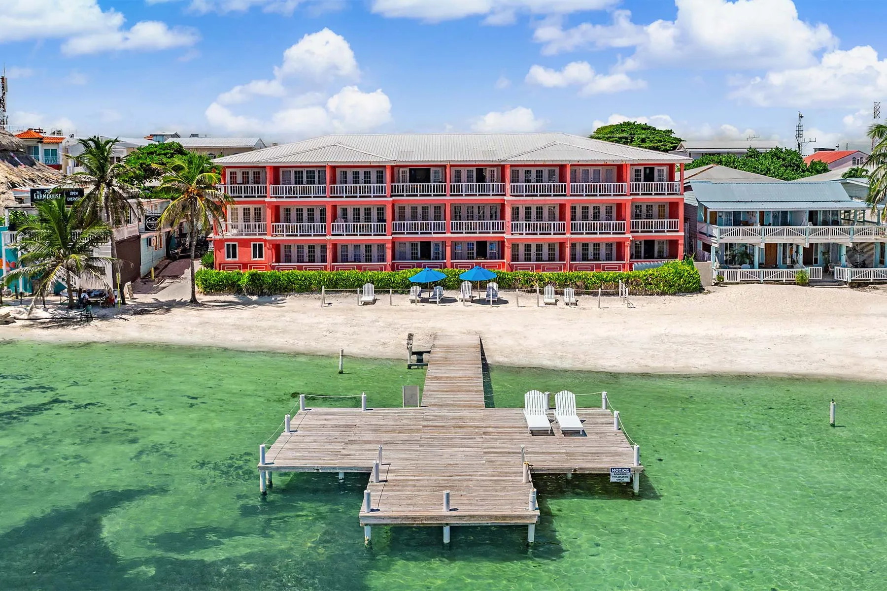 Espacio representativo del hotel: Un hotel frente a la playa se alza detrás de un muelle de madera sobre aguas claras.