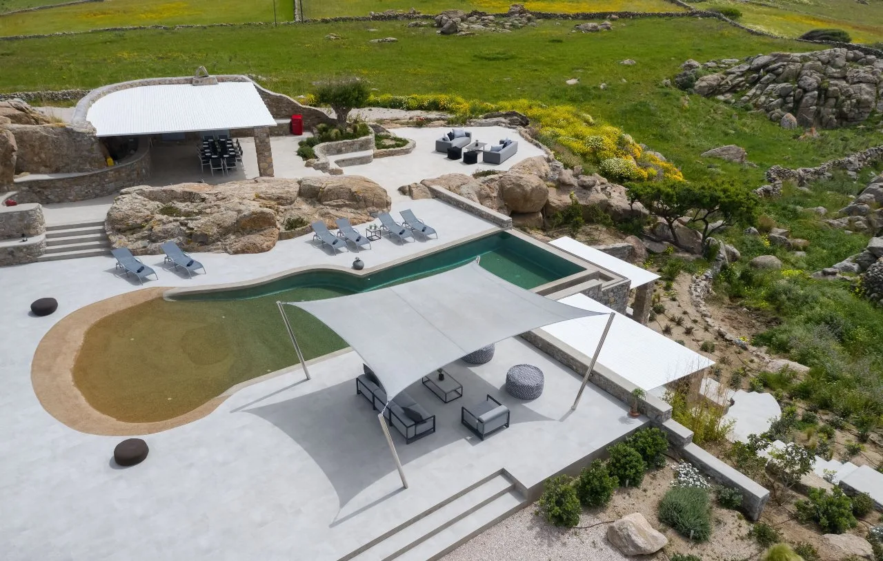 An outdoor pool and patio sit beside a rocky green landscape.