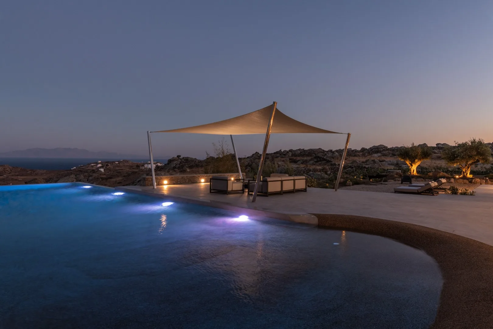 An outdoor pool beside a shaded lounge area at dusk.