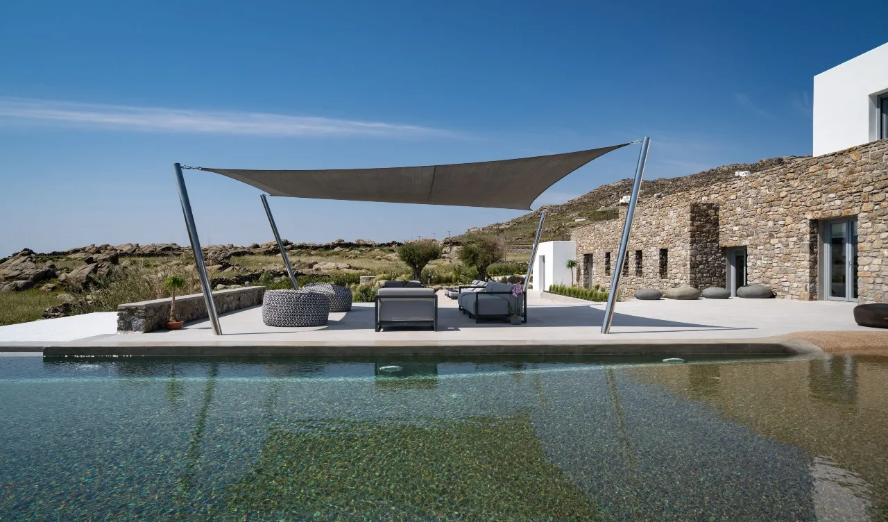 An outdoor pool beside a stone building, with shaded seating on the deck.