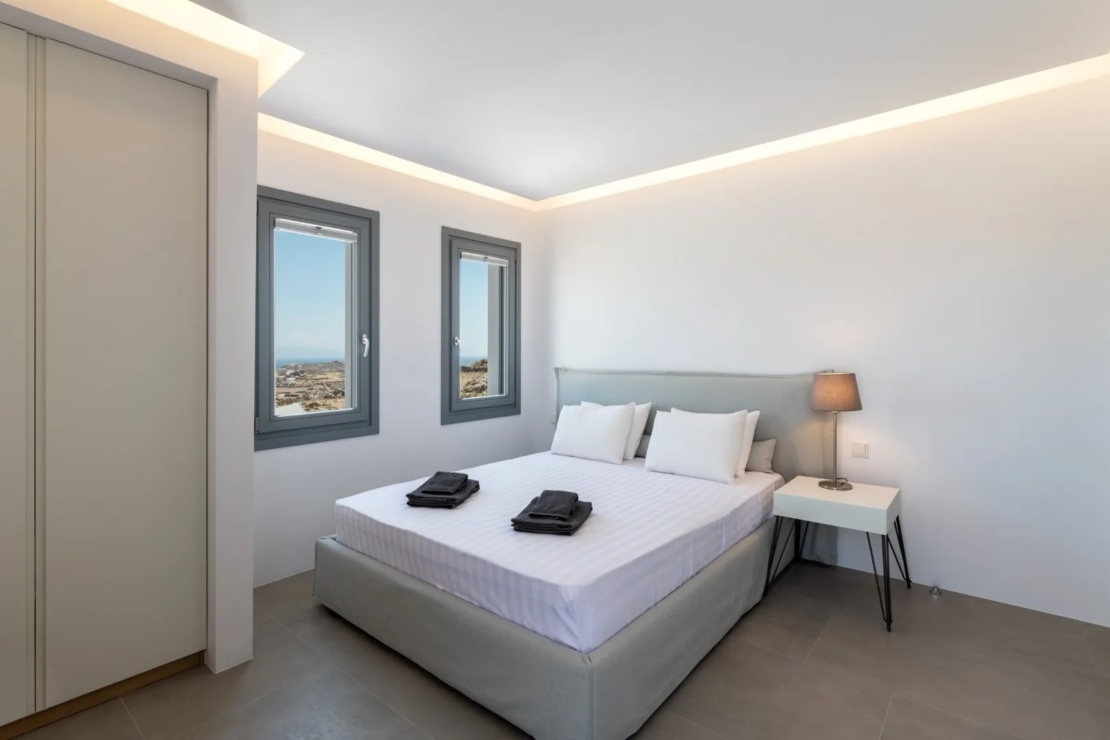 A bedroom with a bed, two windows, and a bedside table.