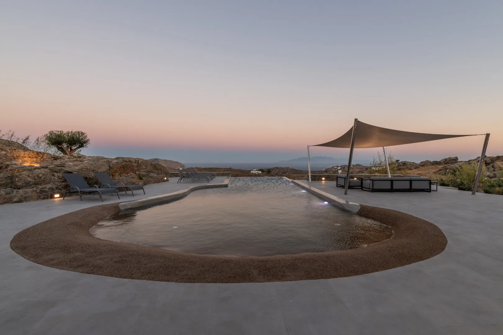 An outdoor pool sits beside a shaded seating area at dusk.