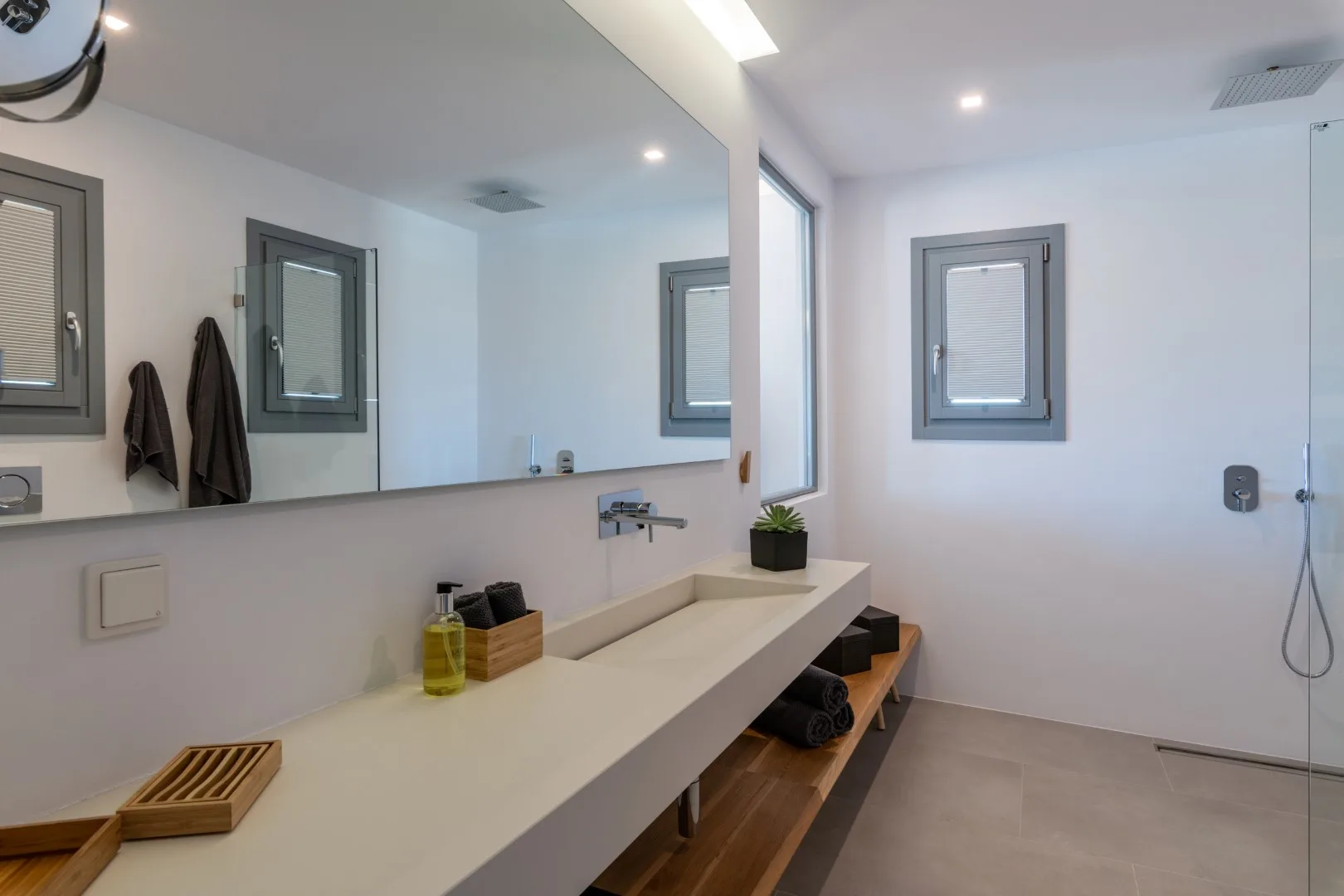 A modern bathroom with a long counter, wall mirror, and shower.