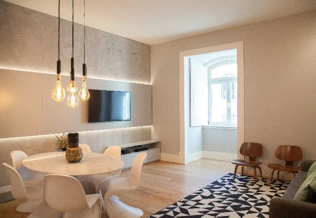 A dining and sitting area with a round table, pendant lights, and a patterned rug.