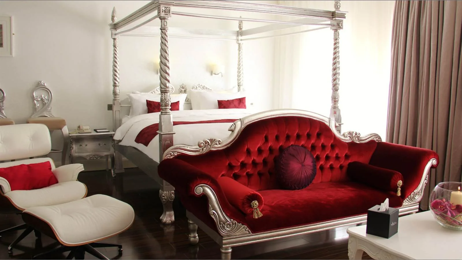 Espacio representativo del hotel: Un dormitorio con una cama con dosel y un diván rojo ornamentado.