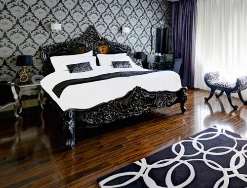 Espacio representativo del hotel: Dormitorio con una cama oscura ornamentada y papel tapiz estampado.